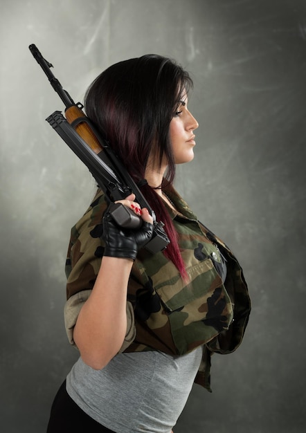 Profilo di una giovane donna attraente in camicia mimetica militare con un Kalashnikov in mano.