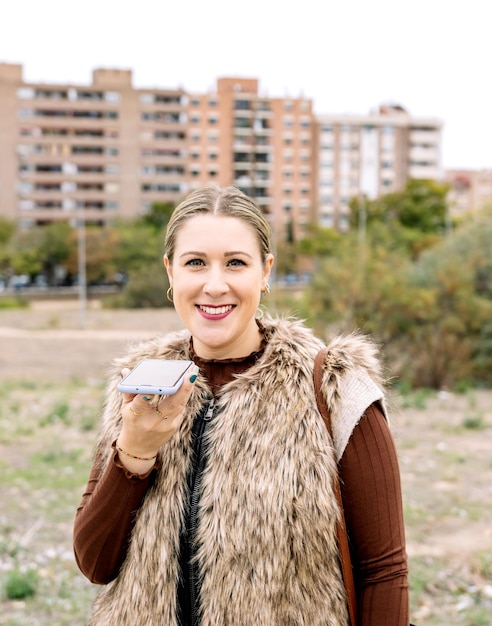 Profilo di una giovane donna sorridente che invia un messaggio vocale con lo smartphone