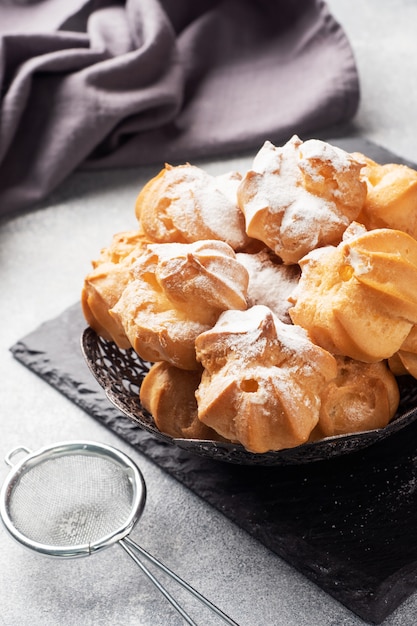 Profiteroles con crema pasticcera e zucchero a velo su un piatto. Tavolo grigio cemento. Copia spazio.