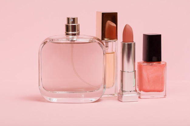 Profumi da donna, rossetto e bottiglia con smalto per unghie in uno sfondo rosa. Cosmetici e profumi da donna.