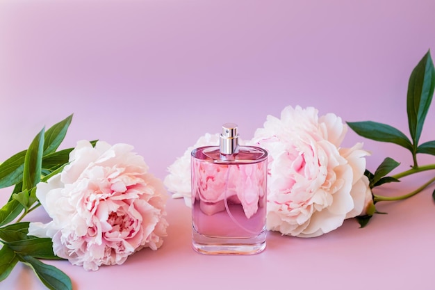 Profumi di cosmetici naturali in una bottiglia di vetro su sfondo rosa e delicati fiori di peonia l'aroma del profumo femminile spazio per il testo