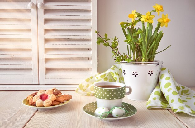 Progettazione della cartolina d'auguri di primavera con i narcisi, il caffè e i biscotti gialli su legno leggero