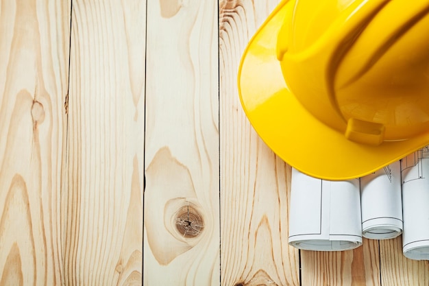 Progetti arrotolati e casco da costruzione giallo su tavole di legno