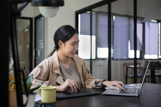 Progettista asiatico della donna che lavora con il computer portatile del computer in ufficio.