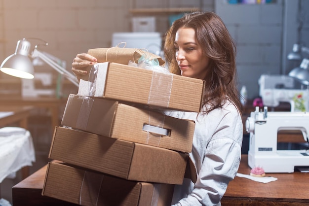 Progettista che tiene una pila di contenitori di regalo del mestiere che stanno nell'officina di cucito