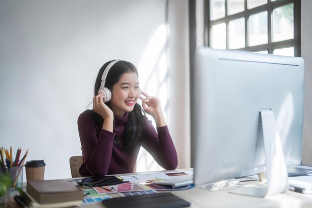 Progettista grafica donne freelance che indossano le cuffie per ascoltare musica per rilassarsi dopo aver disegnato il logo del marchio e lavorare alla progettazione su progettazione grafica con attrezzature tecnologiche in studio domestico