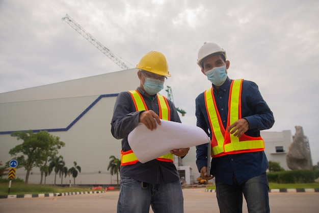 Progetto di lavoro di squadra di due ingegneri durante la costruzione del sito, maschera facciale da indossare per proteggere il covid19, architetto professionista del lavoro dei lavoratori