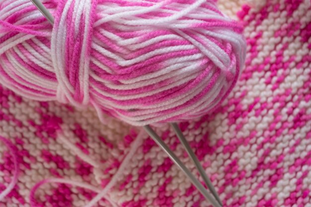 Progetto di maglieria in corso Un pezzo di maglia con gomitolo rosa e bianco e ferri da maglia Copia spazio per la pubblicità del logo del testo