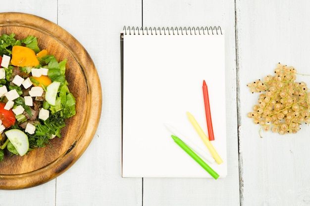 Programma di dieta un'insalata di verdure fresche e un taccuino in bianco su un tavolo di legno bianco