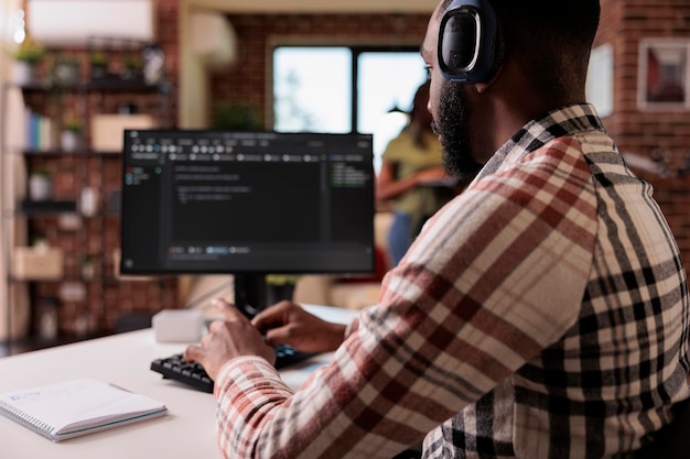 Programmatore afroamericano con cuffie wireless che ascolta musica mentre scrive codice sul personal computer. Programmatore freelance che sviluppa software mentre si ascolta la radio online sull'auricolare.