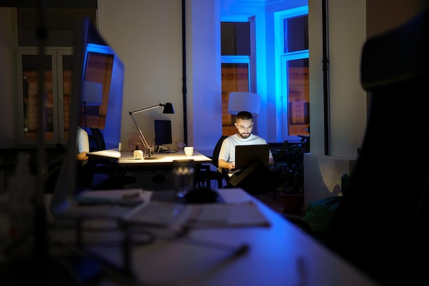 Programmatore insonne che lavora al portatile di notte giovane specialista in occhiali con stile di vita notturno