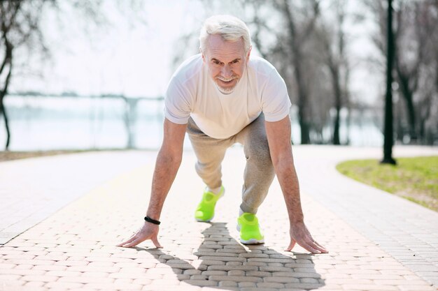 Pronti partenza via. Uomo maturo entusiasta che prepara prima di correre nel parco