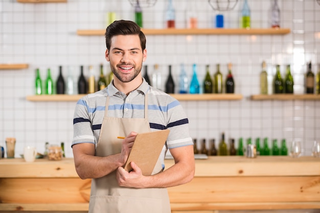 Pronto a lavorare. Cameriere bello bello professionista che tiene i suoi appunti e ti guarda mentre lavora nel bar