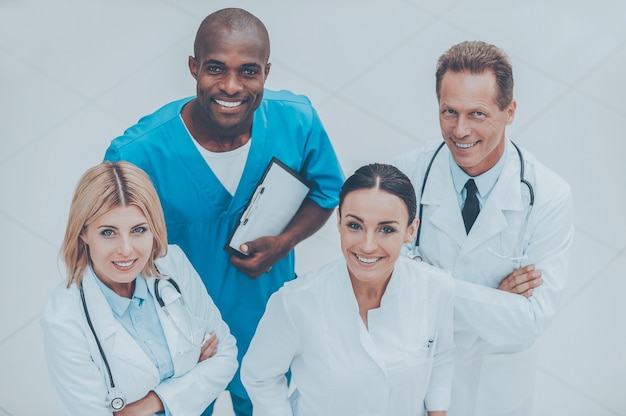 Pronto ad aiutarti in qualsiasi momento. Vista dall'alto di quattro medici fiduciosi in piedi vicini l'uno all'altro e sorridenti