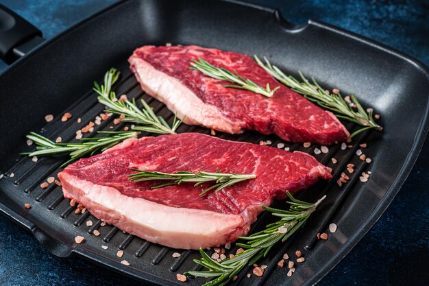 Pronto per cucinare bistecca di manzo cruda o controfiletto in una padella alla griglia Sfondo blu Vista dall'alto