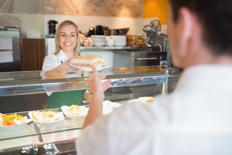 Foto proprietario del negozio femminile dando sandwich al cliente