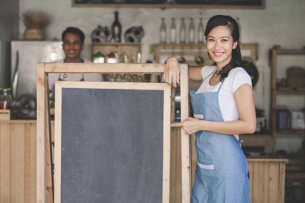 Proprietario femminile asiatico del caffè con il bordo in bianco