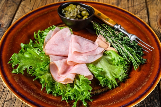 Prosciutto affumicato affettato con insalata fresca e capperi su un piatto. fondo in legno. Vista dall'alto.