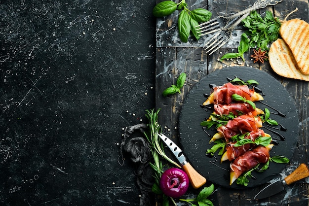 Prosciutto con pere e basilico su una lastra di pietra nera Jamon Antipasto italiano Vista dall'alto