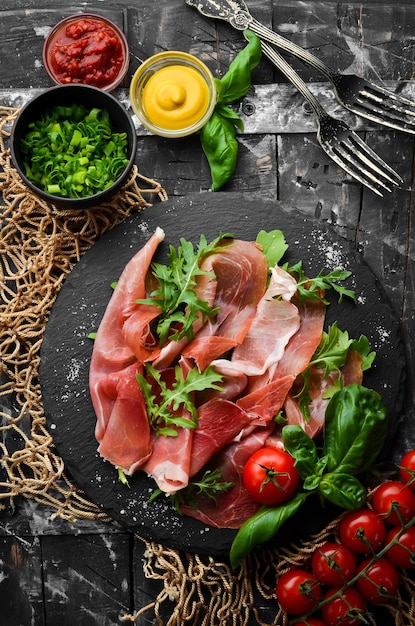 Prosciutto con rucola e basilico su un piatto nero Cucina spagnola Vista dall'alto Spazio libero per il testo