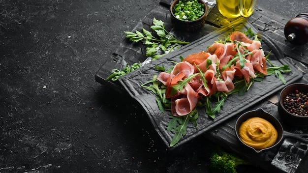 Prosciutto e rucola su una lastra di pietra nera Prosciutto Vista dall'alto Spazio libero per il testo