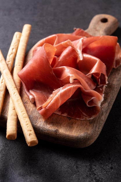 Prosciutto serrano spagnolo con olive e grissino su sfondo nero