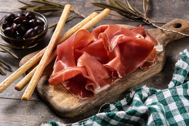 Prosciutto serrano spagnolo con olive e grissino su tavola di legno