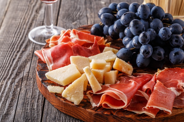 Prosciutto, vino, uva, parmigiano sul tavolo di legno.