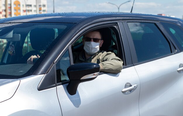 Proteggiti dal coronavirus con una maschera mentre guidi Un guidatore mascherato in un'auto argentata