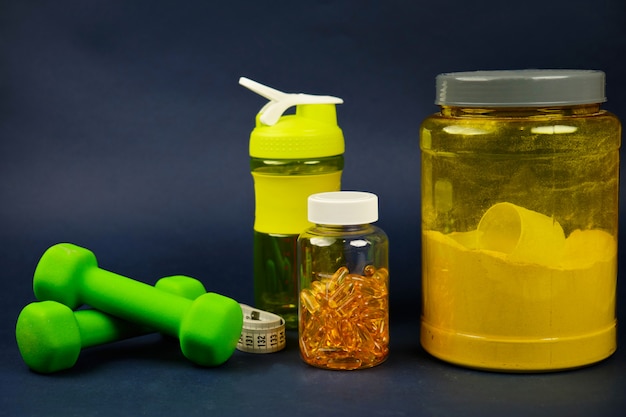 Proteine in un barattolo giallo, shaker di plastica, manubri verdi e un barattolo di omega 3
