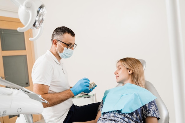 Protesi e impianti dentali Il dentista medico mostra la mascella di plastica artificiale con impianti dentali Consultazione di protesi dentarie con il dentista per la donna paziente in odontoiatria