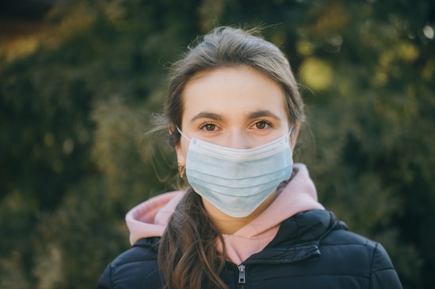 Protezione da portare della ragazza ammalata durante la pandemia. Ragazza caucasica abbastanza giovane che intraprende maschera medica all'aperto. Ragazza che indossa una maschera medica durante l'epidemia di Coronavirus COVID-19.