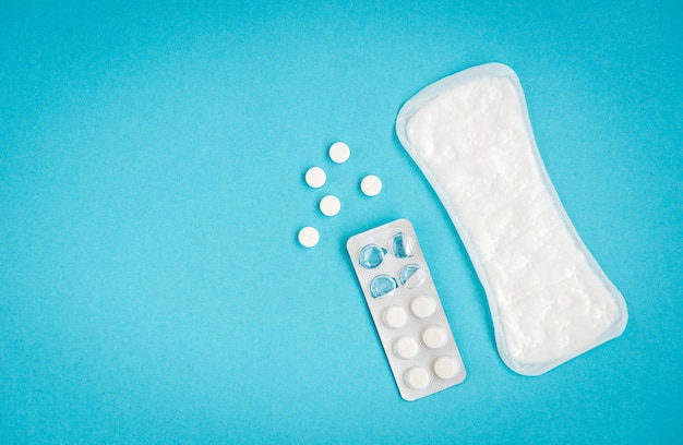 Protezione igienica della donna. Assorbenti e pillole su sfondo blu.