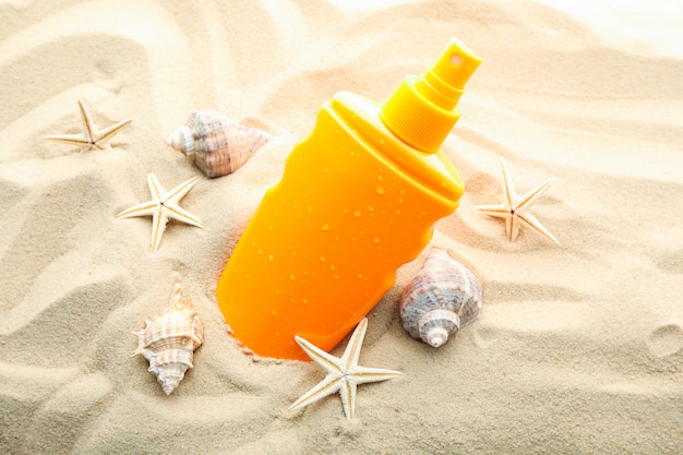 Protezione solare con le stelle marine e le conchiglie su chiara sabbia di mare, primo piano e spazio per testo. Vacanze estive