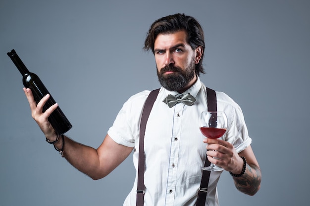 Prova questo elegante uomo d'affari indossare papillon per eventi formali sommelier degustazione di alcolici barista elegante barman maschio che beve bicchiere di vino uomo con la barba in bretelle bere vino rosso