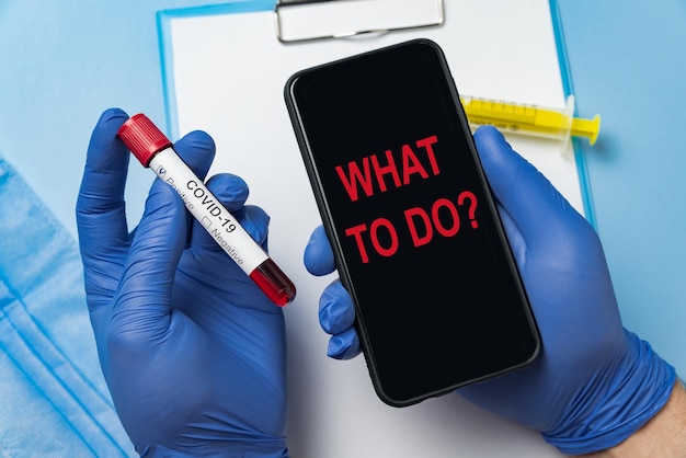 Provetta con sangue con etichetta Covid19 e smartphone con scritta sullo schermo Cosa fare Coronavirus 2019nCov