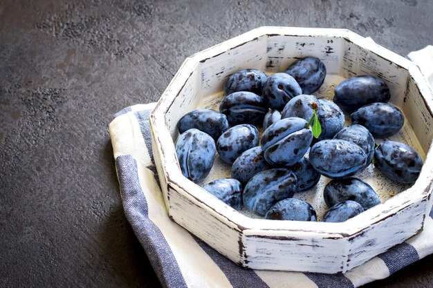 Prugna blu scuro in vassoio bianco su un primo piano nero del fondo