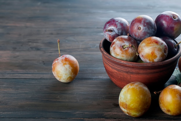 Prugne fresche dal giardino in ciotola sulla vecchia tavola di legno.