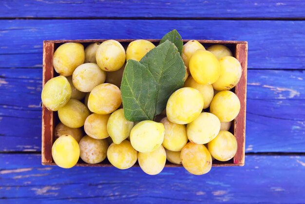 Prugne gialle fresche Frutti maturi in una scatola di legno su sfondo blu