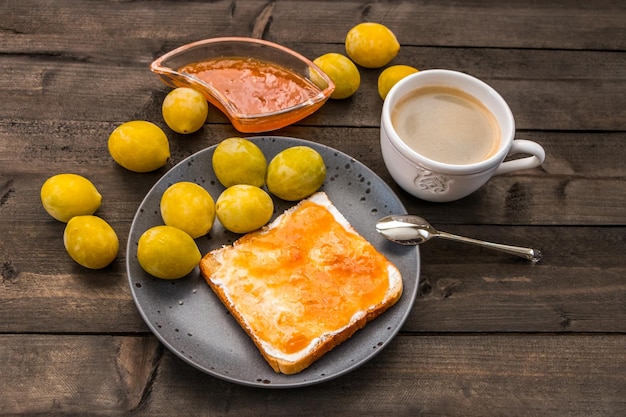 Prugne gialle su un tavolo di legno Toast con marmellata di prugne su un piatto e una tazza di caffè