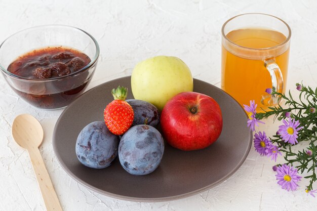 Prugne mature raccolte, mele, una fragola sul piatto