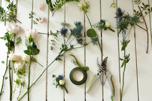 Pruner e altri strumenti del fiorista e fiori freschi tagliati che si trovano sulla tavola di legno bianca.