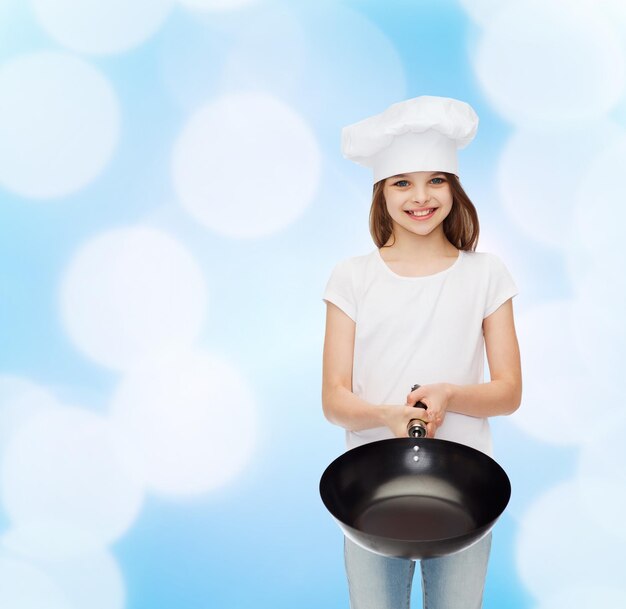 pubblicità, infanzia, cucina e persone - ragazza sorridente in maglietta bianca e cappello da cucina che tiene padella su sfondo blu