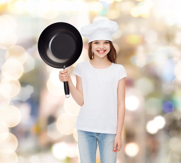 pubblicità, infanzia, cucina e persone - ragazza sorridente in t-shirt bianca e cappello da cucina che tiene padella su sfondo vacanze