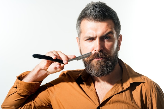 Pubblicità per barbiere. Bel ragazzo barbuto tiene un pericoloso rasoio vicino al viso. L'uomo del barbiere con la barba, i baffi tiene il rasoio. Macho barbuto da barba con lametta. Copia spazio per pubblicizzare