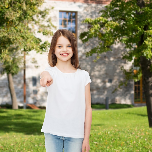 pubblicità, vacanze estive, gesti, infanzia e persone - ragazza sorridente in maglietta bianca che punta il dito su di te sullo sfondo del campus