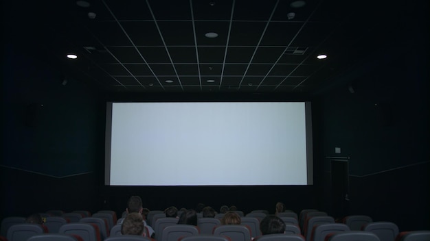 Pubblico nella sala cinematografica che guarda lo schermo bianco in attesa dello spettacolo cinematografico