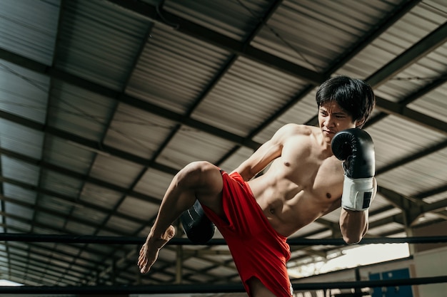 Pugile aggressivo in guantoni da boxe fa calci al ginocchio sul ring di boxe nella sala di allenamento di boxe