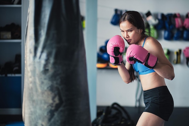 Pugile femminile che colpisce un sacco da boxe con i guantoni in palestra