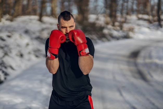 Pugile forte con guantoni da boxe in piedi nella natura durante una giornata invernale innevata e sparring. Boxe nella natura, vita sana, sport invernali